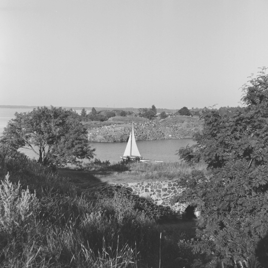 Mustavalkoinen kuva vuodelta 1955. Pieni purjelaiva kulkee Suomenlinnan väylässä. On kesä. Kuvaaja Volker von Bonin.
